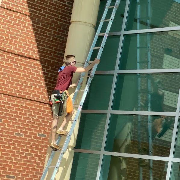 Dylan Lee Jones on a ladder cleaning commercial glass