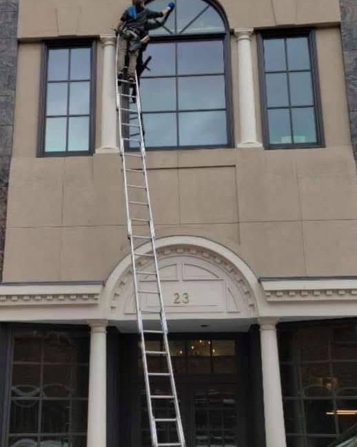 Dylan on a tall ladder at an arched storefront window downtown